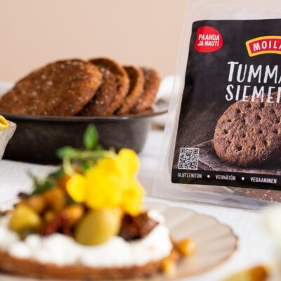 Kuvassa Moilasen suojakaasuun pakattu leipäpakkaus Tumma & Siemenet, ja etualalla sama leipä täytettynä fetavaahdolla ja paahdetuilla kikherneillä.