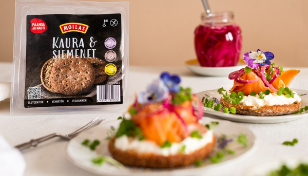 Kuvassa näkyy Moilasen suojakaasuun pakattu Moilas Kaura & Siemenet leipä, ja etualalla kyseinen leipä on täytetty kylmäsavulohella ja tuorejuustolla. 